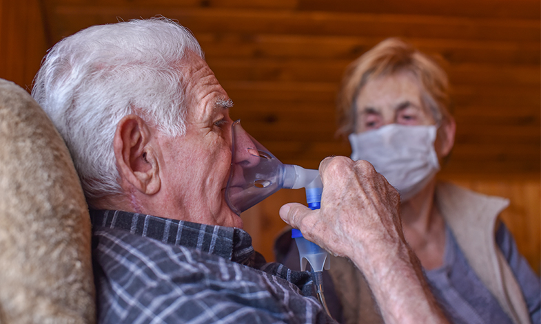 An image of a respiratory patient with an oxygen mask, sat with another who is wearing a face mask.