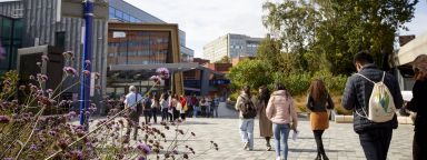 Students walking on the concourse outside the Student's Union on a sunny day.