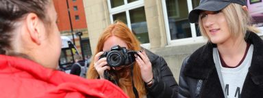 Two journalism students interviewing a member of the public, using a camera and mic