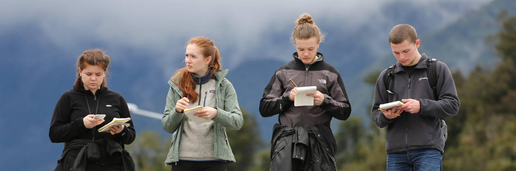 Four students study their notes during fieldwork in New Zealand