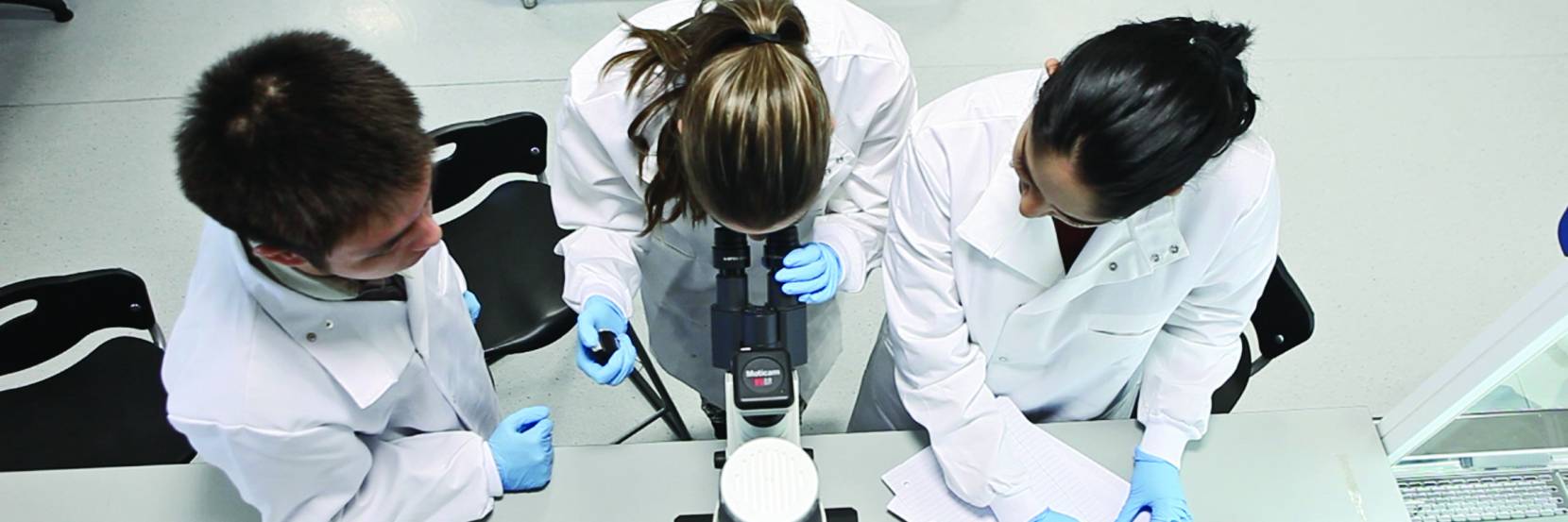 Three bioengineering students working around a microscope and taking notes