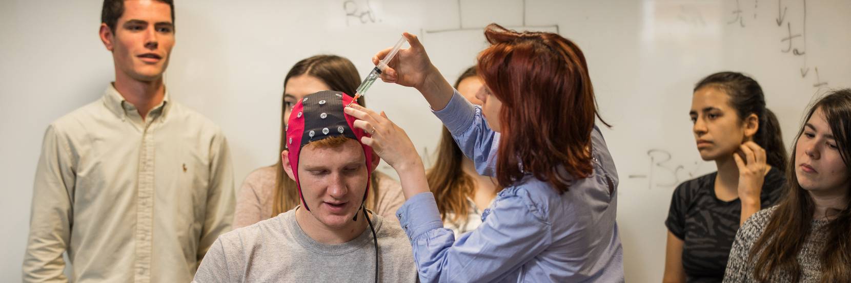 Lecturer demonstrating an EEG is a test to a class. A student wears a headpiece used to evaluate the electrical activity in the brain