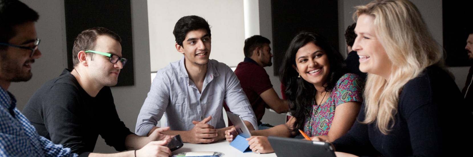 5 students sitting around a desk doing group work in a seminar room