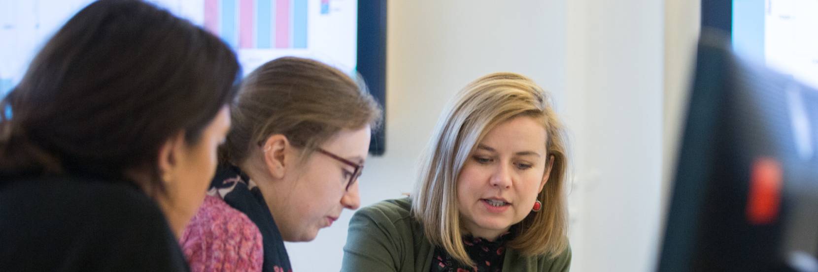 Teacher sat with students working through a textbook in front of a computer