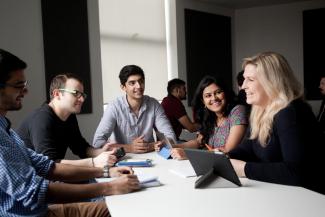 Image of five postgraduate management students with tablets sitting around a white table