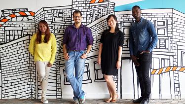 Four international students lean against a wall.