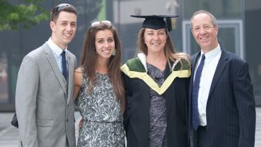 Mature student poses for camera with family at graduation