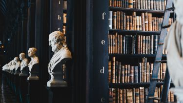 Image of shelves in a library with busts of philosophers in front