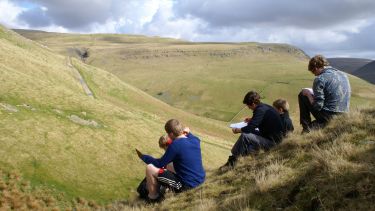 Geograpghy students sat on a hill during a fieldtrip taking notes - image