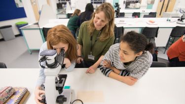 DLL tutor in lab with students using a microscope 