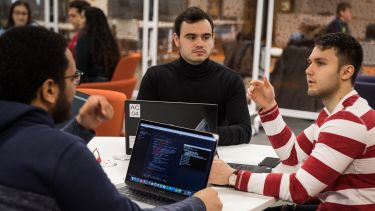 Undergraduate students in discussion with laptops.