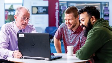 Postgraduate students sat around a laptop with a tutor discussing work