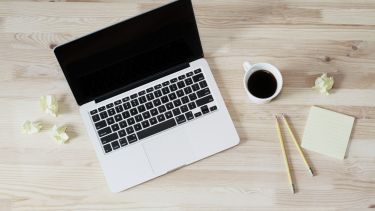 laptop on a desk, with coffee & notepad