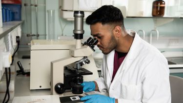 A male research student looking down a microscope