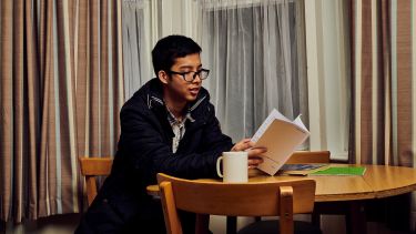 A boy reading a book and having a hot drink in the kitchen of crewe lodge 