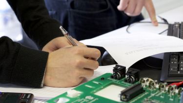 An image of student hands writing next to circuit board