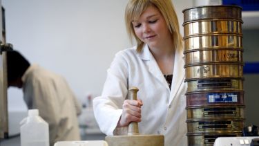A woman in a lab coat using a pestle and mortar