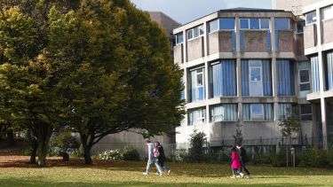 Some students walking on a grassy path with the Geography building in the background behind them.