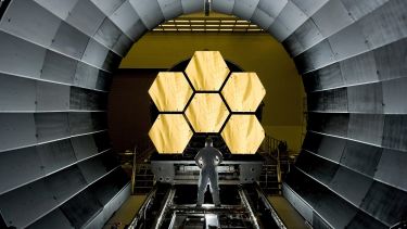 A worker looking at six hexagon mirrors in a space telescope.