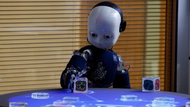A little robot with a white face interacting with a cube.