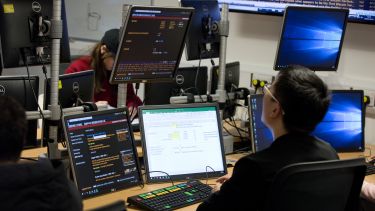 A student using a computer with three screens in the Management School trading room