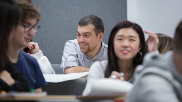 A male students looks over notes while in class. Other students can be seen in the foreground.