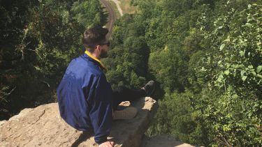 Lewis sits on a rocky outcrop overlooking a forest