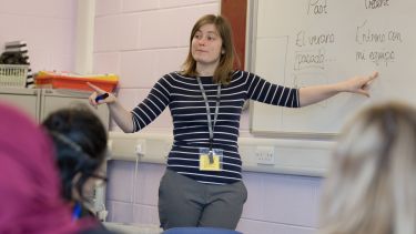 A PGDE student is at the front of a classroom, asking their pupils questions about the work on a white board - image