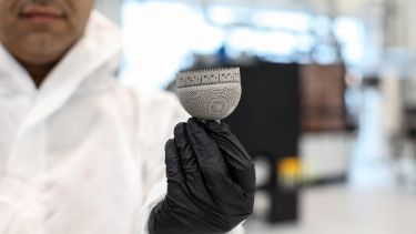 An engineer in full protective clothing holding a 3D-printed lattice hip joint