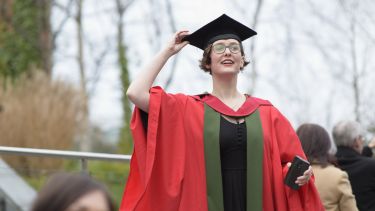 A female graduate in red robes looking into the distance.