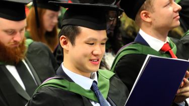 A male student reads his souvenir programme at the undergraduate graduation ceremony.