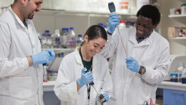 Three Medical School students conducting lab research. They are wearing lab coats. 