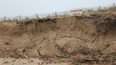 An eroded sand dune with a warning sign on it