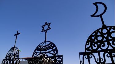 Three iron gates topped with a crucifix, star of David and a crescent moon.