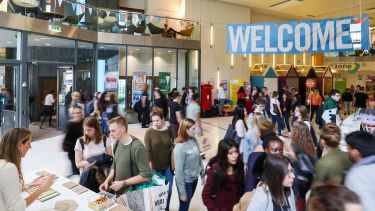 A sign reads 'Welcome' inside the Students union. Students visit an information desk.