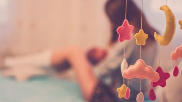 A woman breastfeeds her baby. She is in the background behind a moon and stars hanging baby toy.