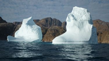 Two tall icebergs standing against a rocky shore