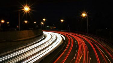 A motorway at night. The vehicle lights are blurry, representing speed. 