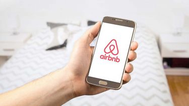 A hand holding a mobile phone with the Airbnb logo on it. 