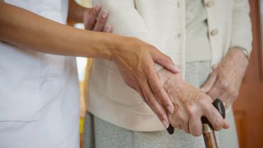A carer with an elderly person holding a walking stick