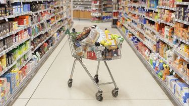 Picture of a trolley full of food in the middle of a supermarket aisle