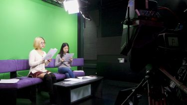 Two students in the green room reading a script ahead of a broadcast.