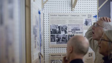 Man stands with hand on head looking at exhibition on squatting