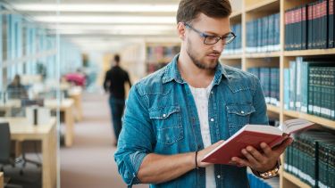 Postgraduate student reading a book stood up in a library