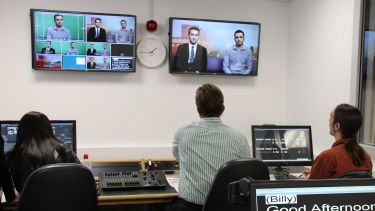 The production studio - we can see the presenters on screen, producers using the equipment and a teleprompter.