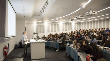 A full room at a presentation for International Journalism Week. Jackie Harrison, Head of School, presents at the front.