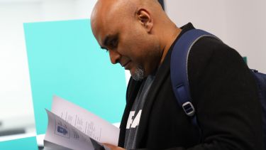 A man attending the Journalism postgraduate research conference. He is reading the conference brochure.