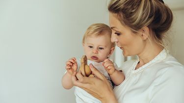 A Mother holding a child, showing them a wooden toy