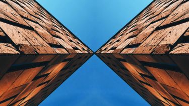 Two buildings intersect at angles against the blue sky