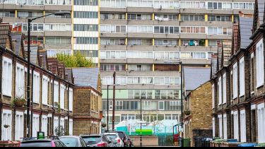 a block of flats overlooks a street with parked cars